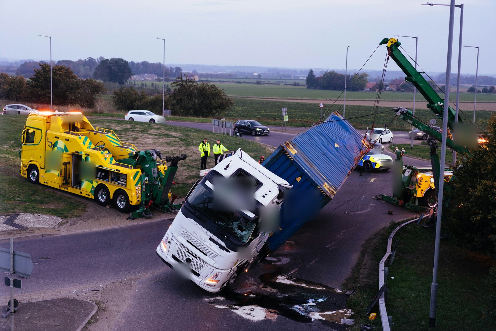 Recovery crews lifting an overturned lorry at a roadside accident at dusk