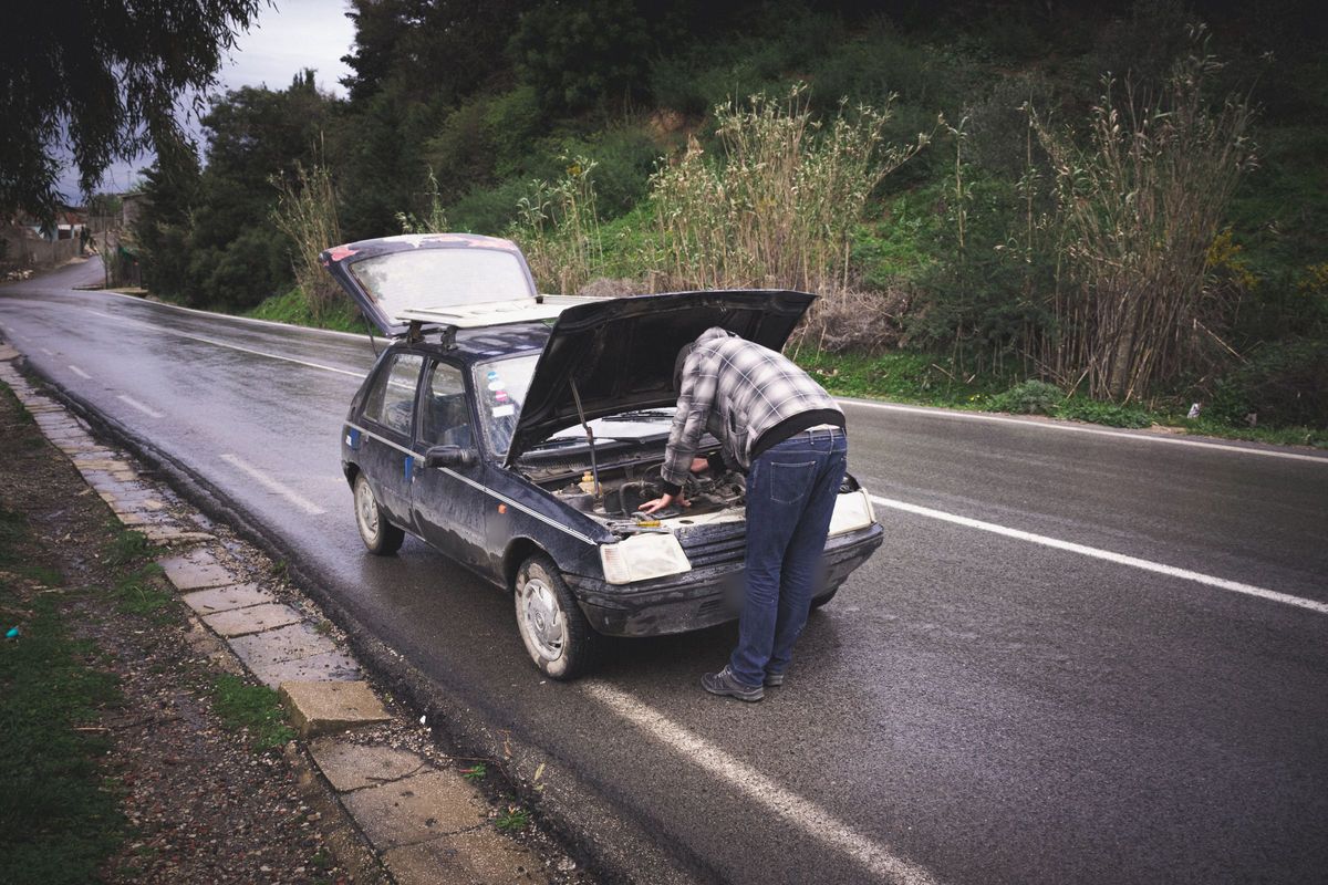 Driver checking under the bonnet of a broken-down car at the roadside