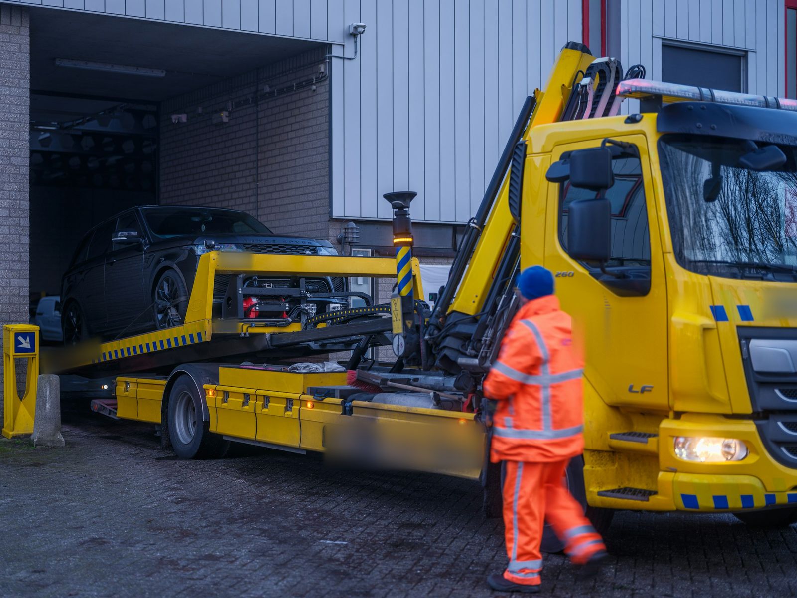 Recovery operator loading a car onto a tilt-and-slide recovery truck at dusk